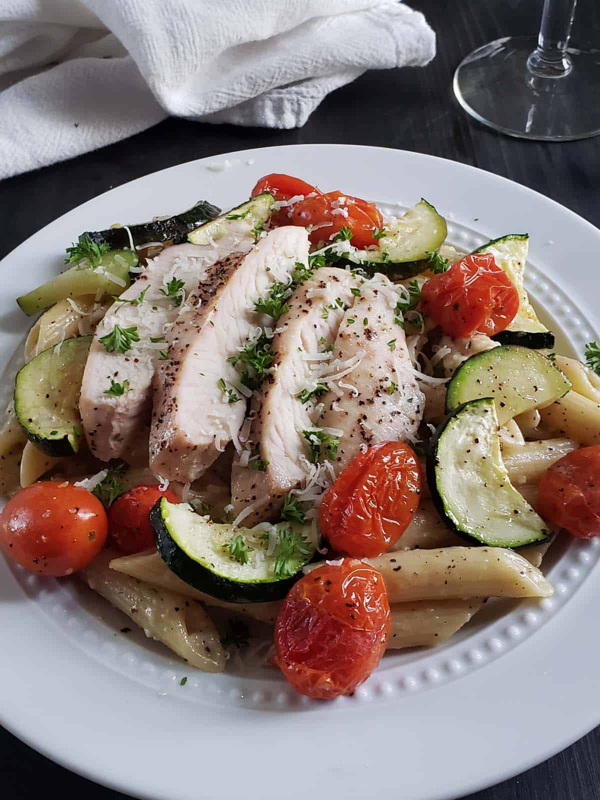 Cacio e pepe with vegetables and chicken on a white plate.
