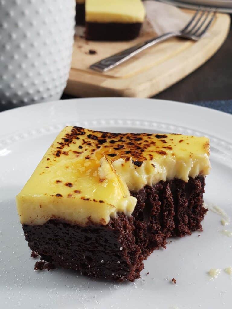 Close up of creme brulee brownie with a bite missing on a white plate.