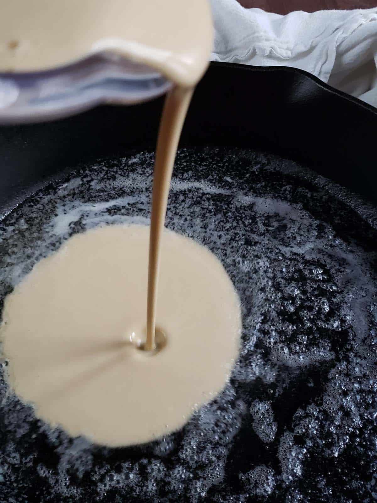 Pouring batter into a cast iron skillet.