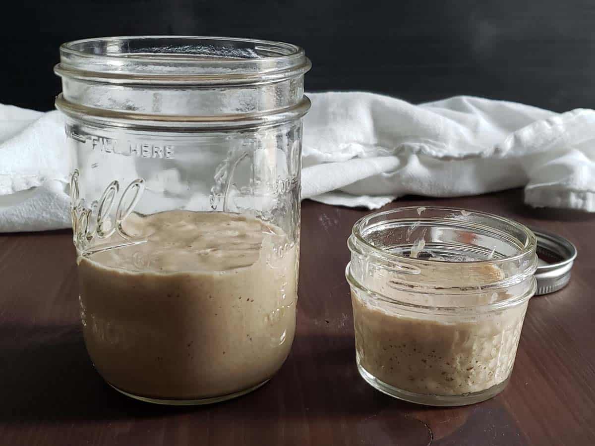 Glass jar of sourdough discard next to a smaller glass jar of sourdough starter.