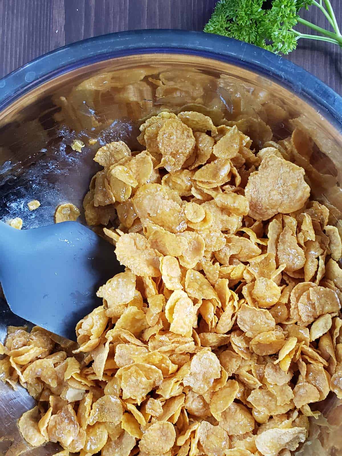 Corn flakes tossed with butter in a metal bowl.