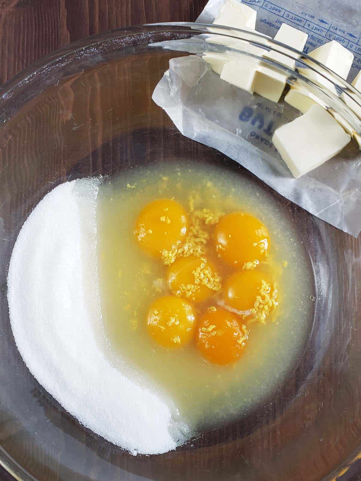 Egg yolks, lemon juice, sugar, and lemon zest in a glass bowl.