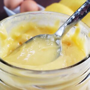 Lemon curd in a glass jar with a spoon stuck in it.