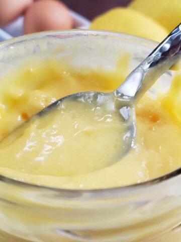 Lemon curd in a glass jar with a spoon stuck in it.