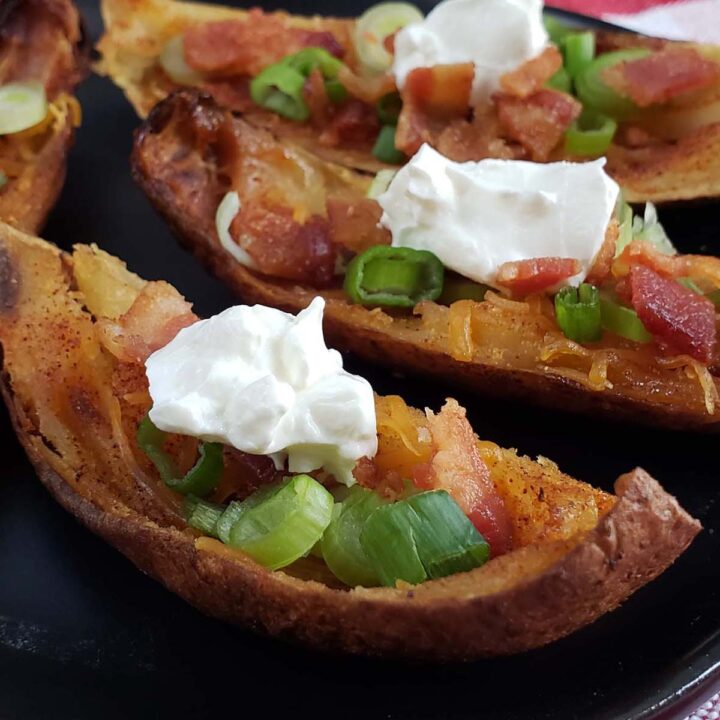 Smoked potato skins topped with green onions, sour cream, and bacon on a black plate.