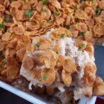 Scooping out casserole from white casserole dish.