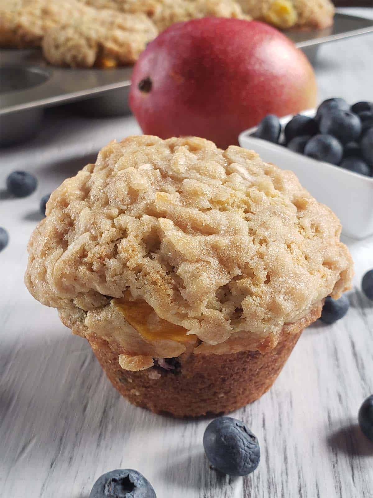 Mango blueberry muffin on a white surface surrounded by blueberries.