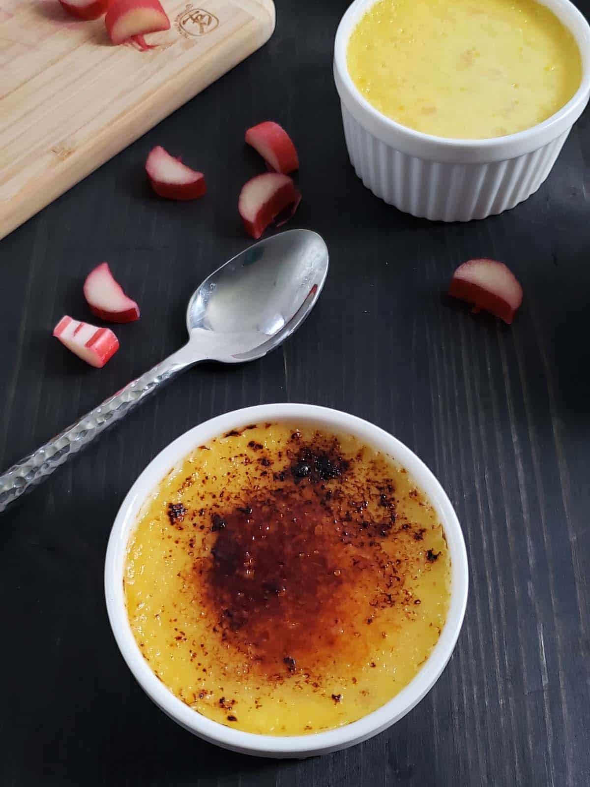 Rhubarb creme brulee on a dark background next to a spoon.