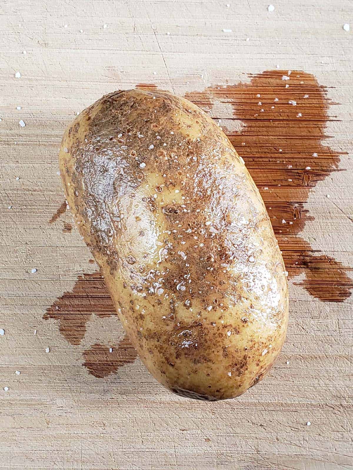 Baking potato rubbed with oil and sprinkled with salt on a cutting board.