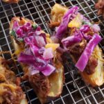 Pulled pork stuffed potato skins topped with coleslaw on a wire rack.