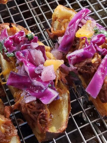 Pulled pork stuffed potato skins topped with coleslaw on a wire rack.