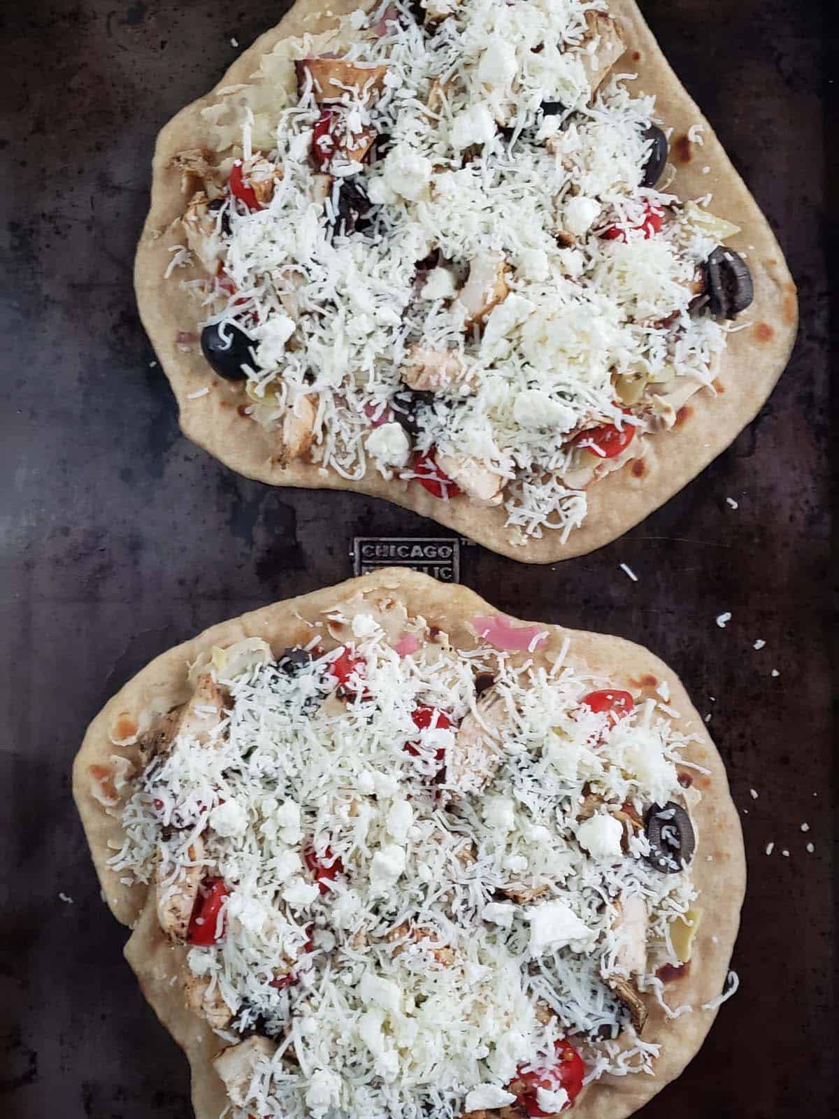 Unbaked Greek chicken flatbread pizza on a metal pan.