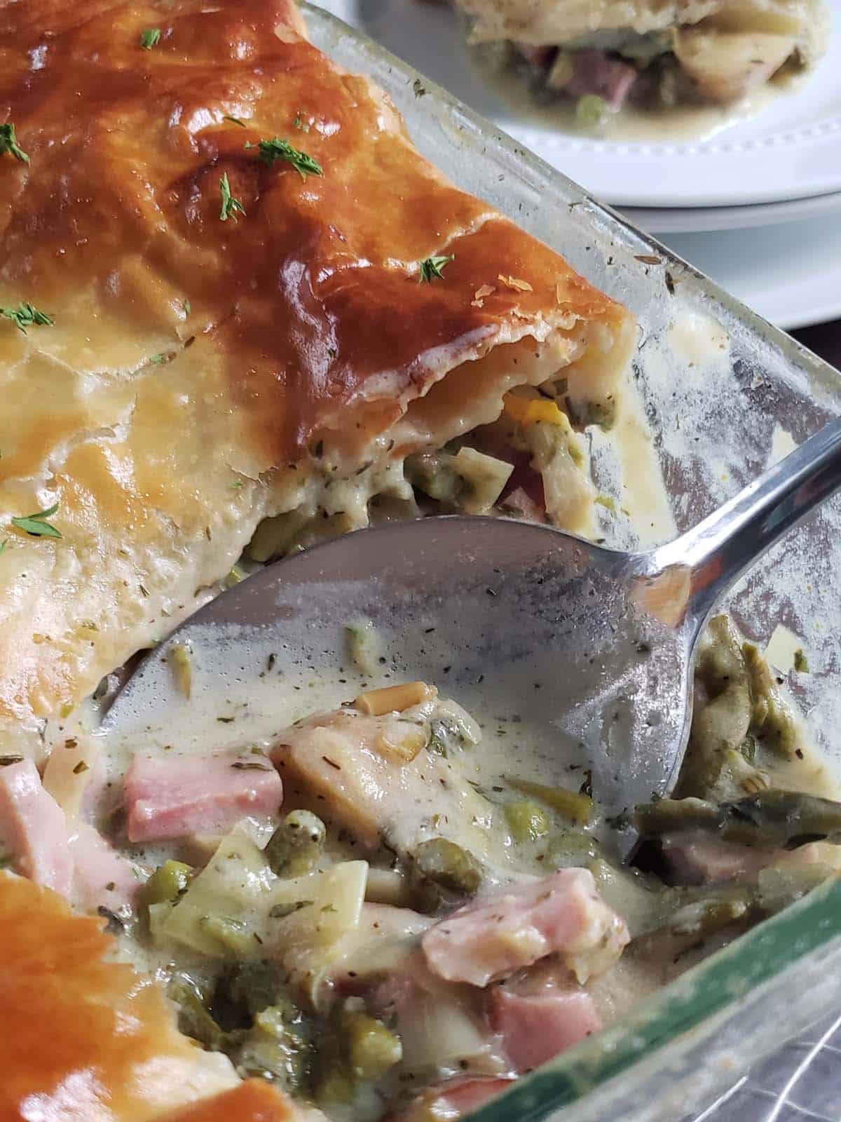 Ham and leek pot pie with a scoop missing in a glass dish.