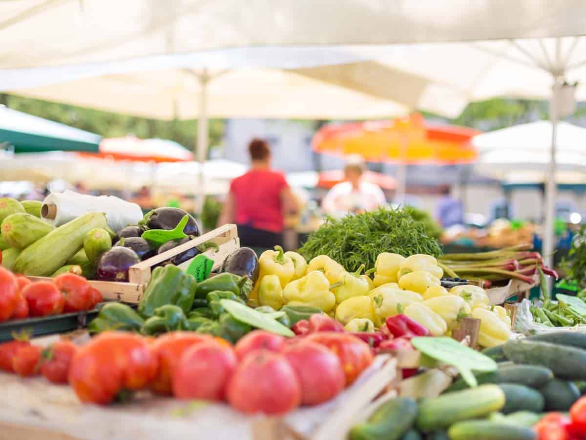 Food market stall with variety of organic vegetable. Vendor serving and chating with customers.