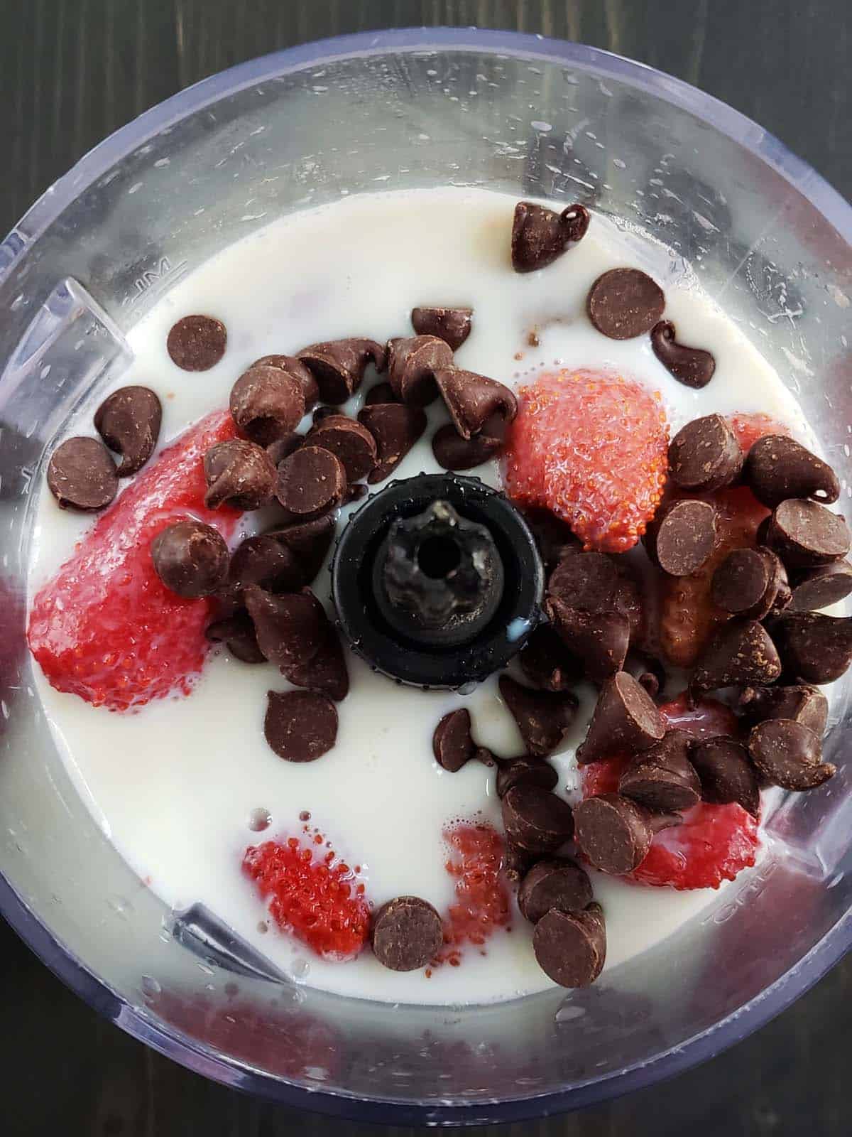 Milk, strawberries, and chocolate chips in a blender.