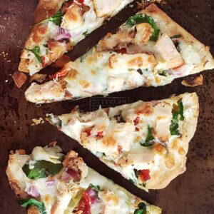 Slices of spinach chicken artichoke flatbread pizza on a baking sheet.