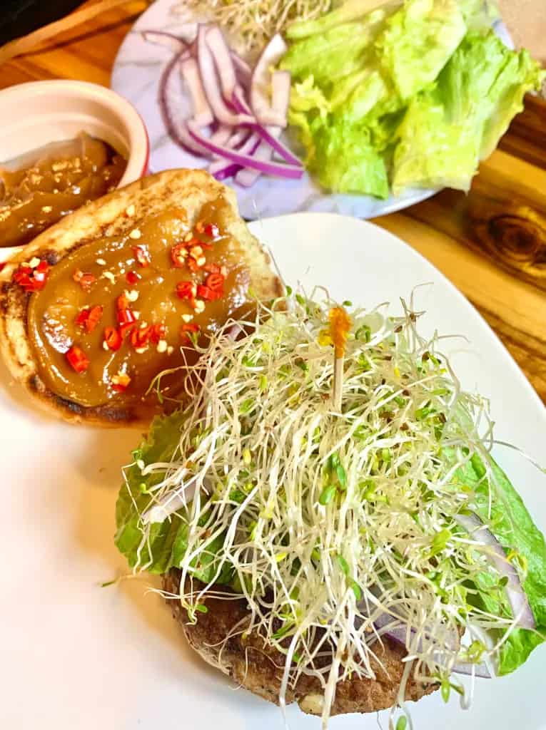 Pork burger topped with sprouts on a white plate.