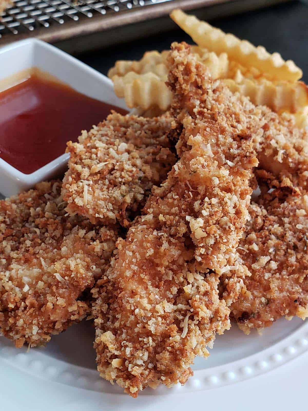 Sourdough chicken strips on a white plate with fries and red dipping sauce.