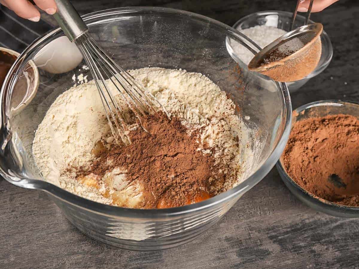 Cocoa powder being whisked into a glass bowl filled with flour.
