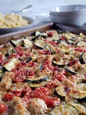 Baked chicken, zucchini, and tomatoes topped with cheese on a baking sheet.