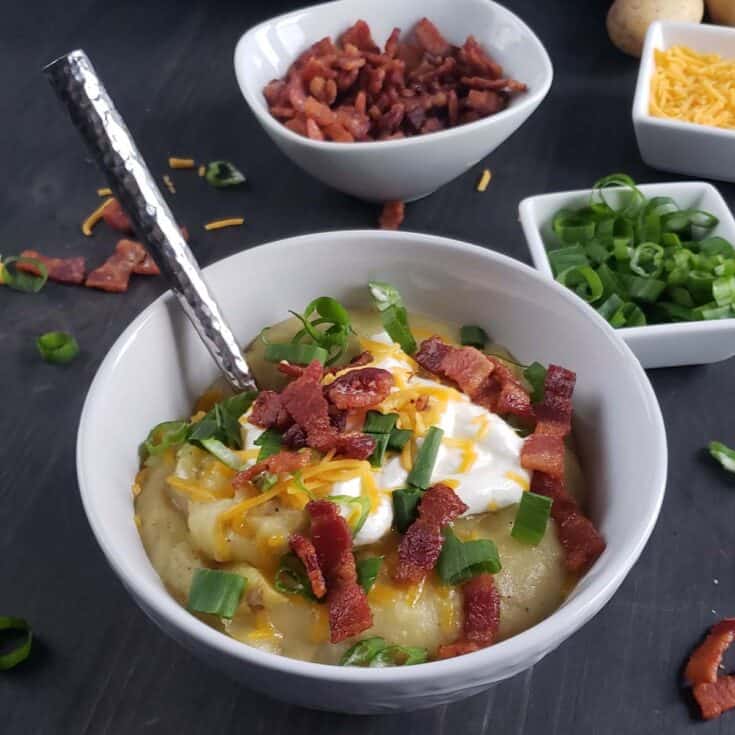 White bowl of potato soup topped with sour cream, bacon, cheese, and green onions.