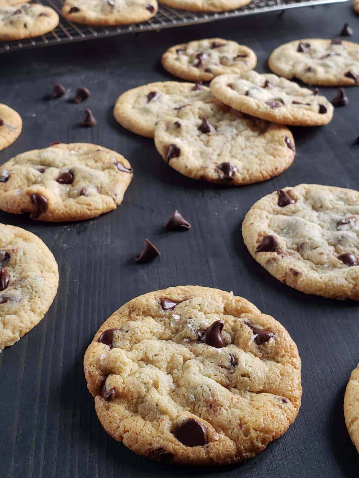 Chocolate chip cookies scattered on a black wood surface.