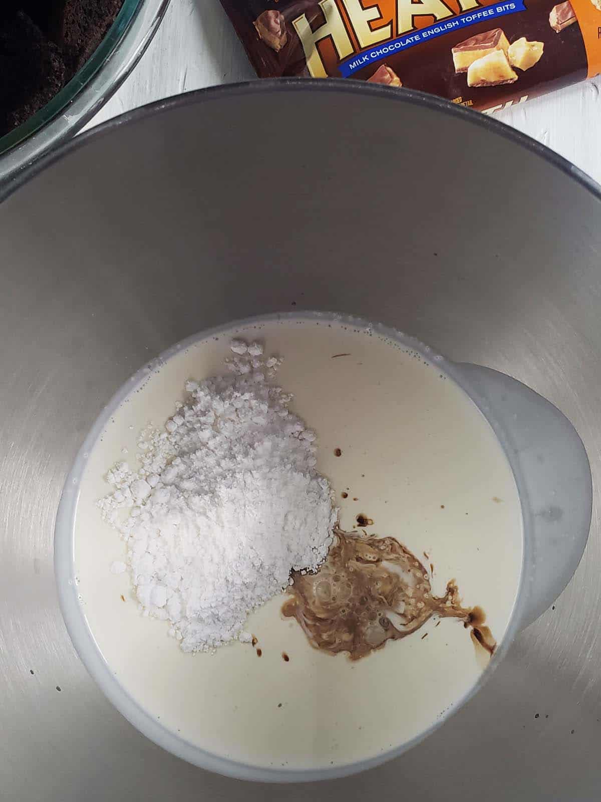 Cream, powdered sugar, and vanilla in a metal bowl.