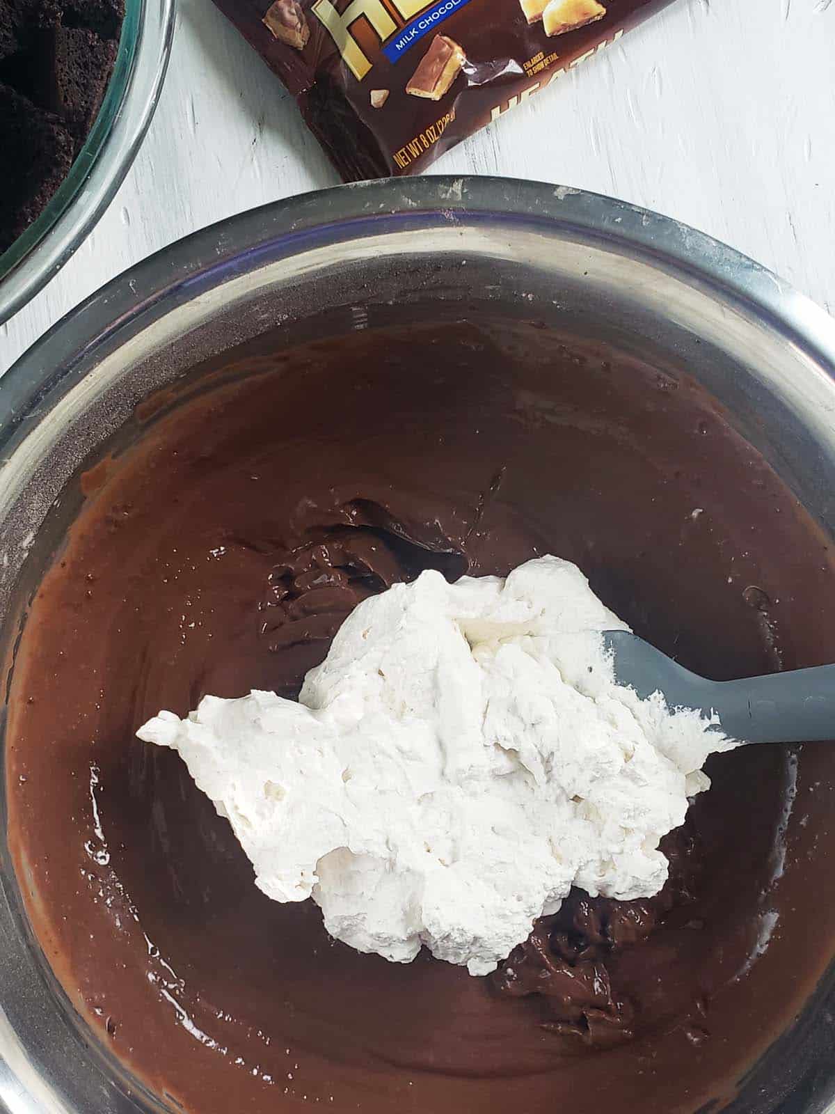 Whipped cream on top of chocolate pudding in a metal bowl.