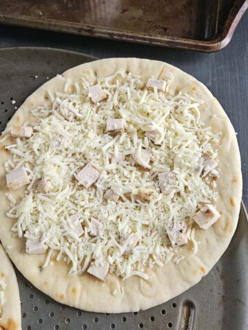Flatbread topped with buffalo sauce, cheese and chicken  on a metal pizza pan.