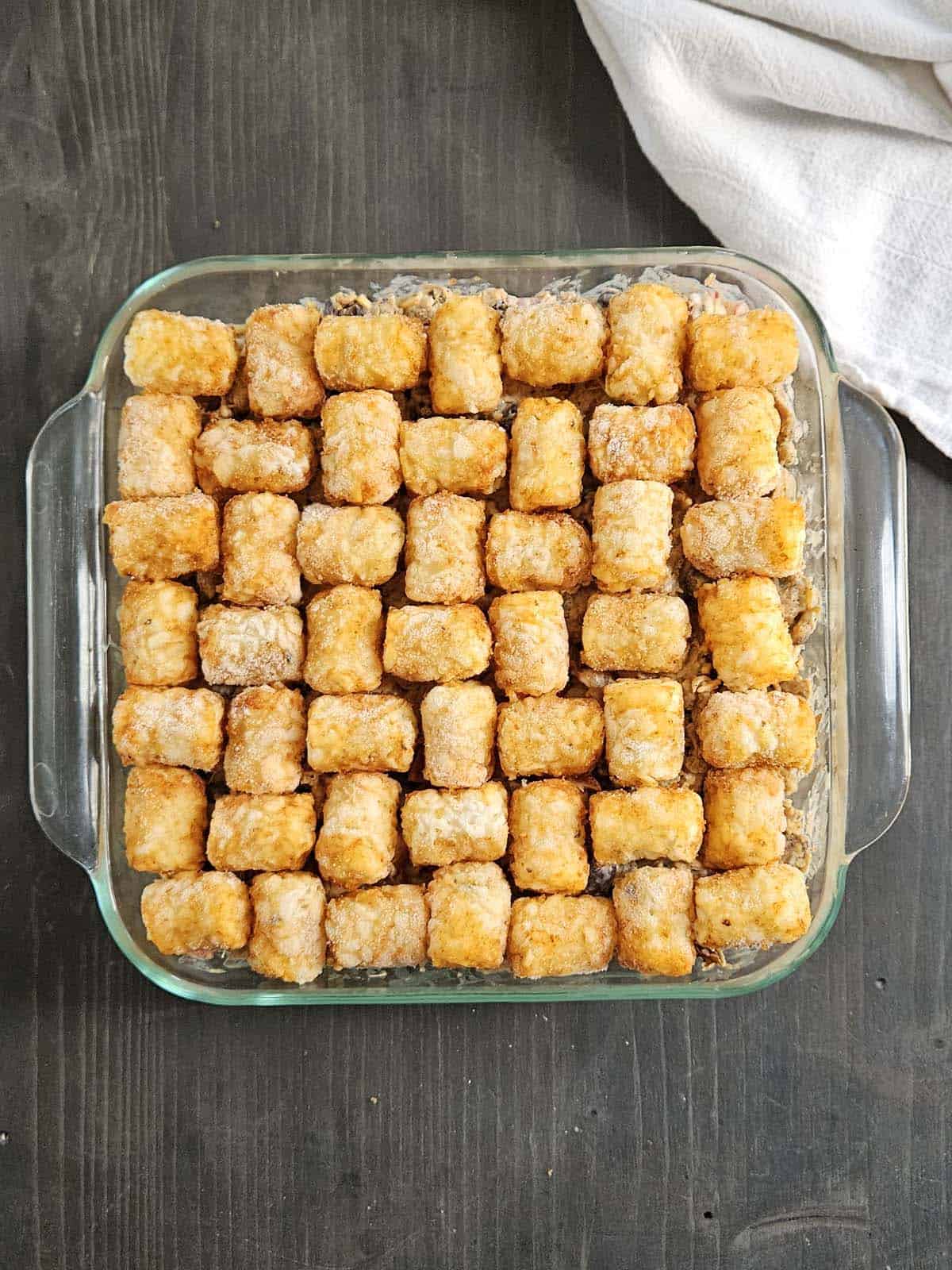 Pork casserole topped with frozen tater tots in a glass casserole dish.