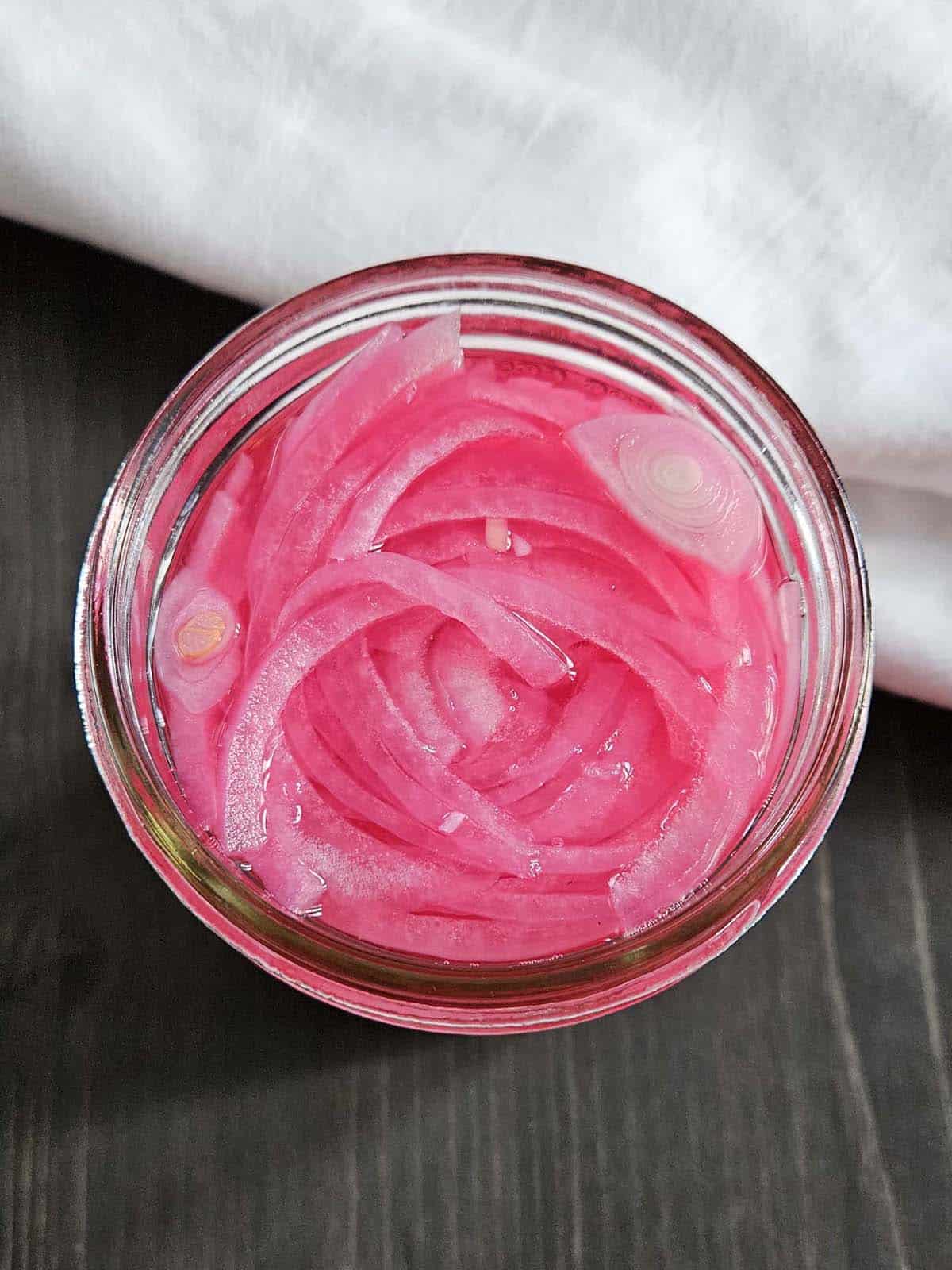 Top down view of pickled onions in a glass jar.