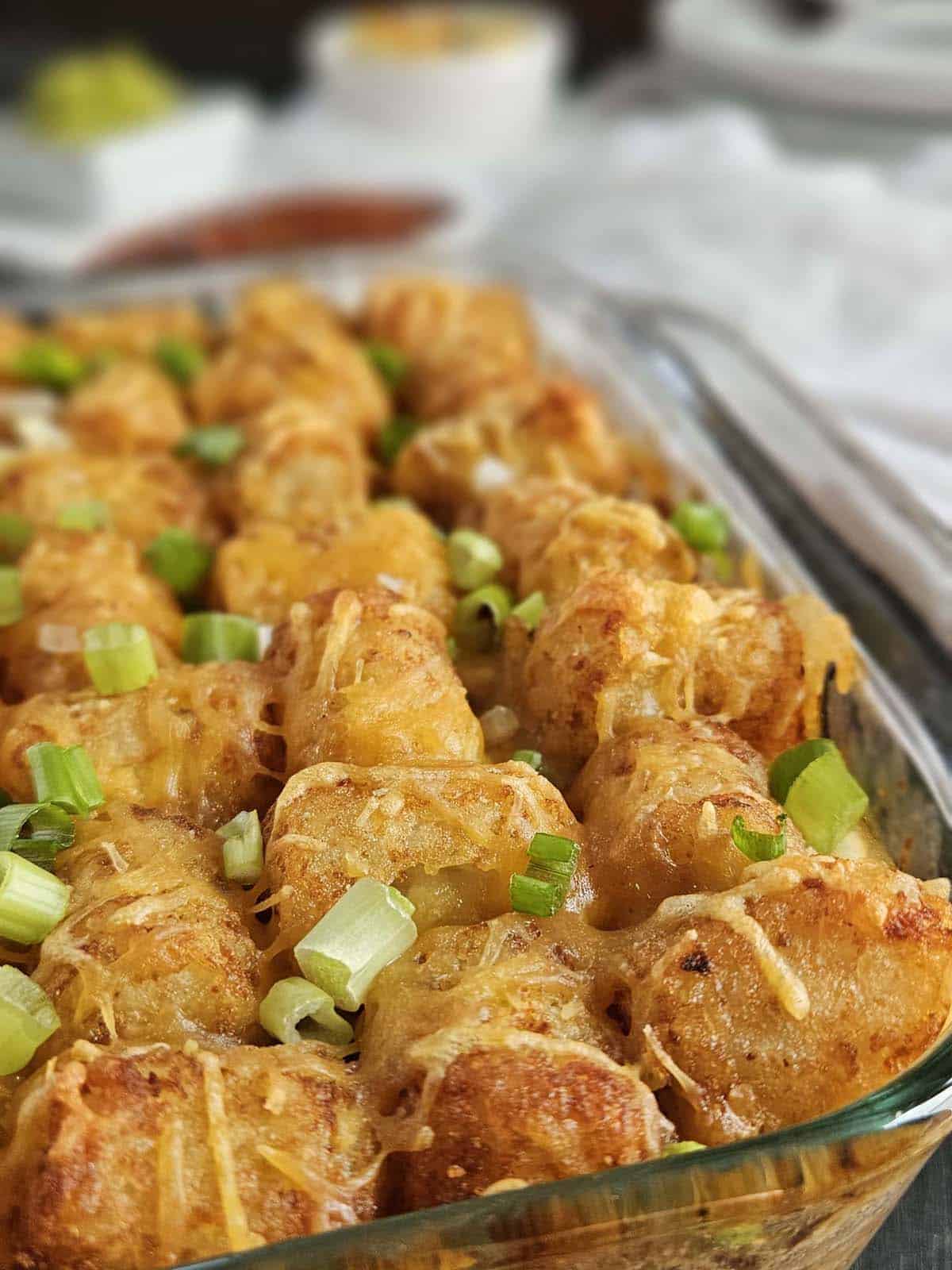 Pork casserole topped with tater tots and green onions in a glass casserole dish.