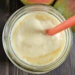 Top down view of a mango smoothie in a glass jar.