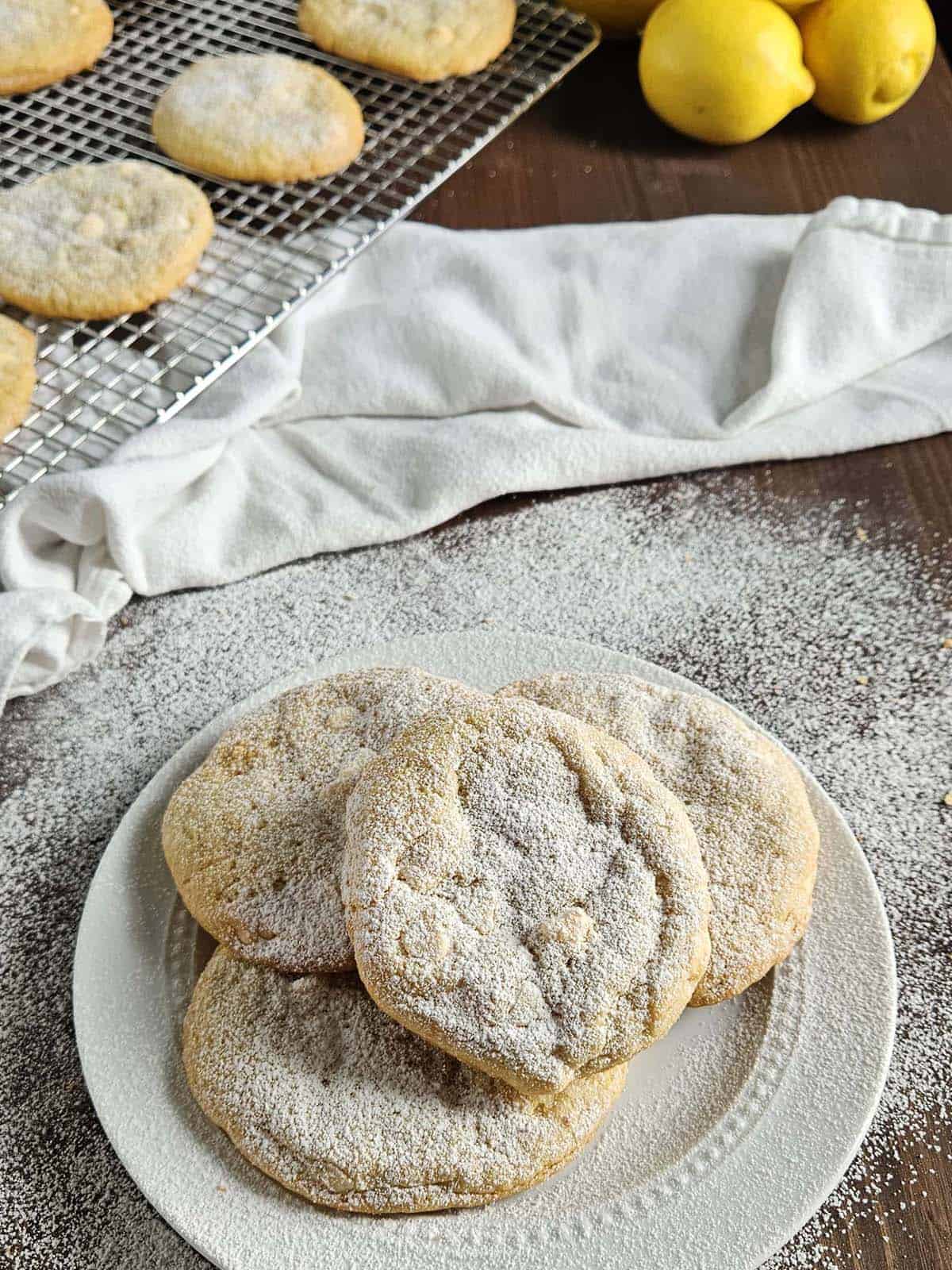 Four lemon cookies topped with powdered sugar, on a white plate, surrounded by more powdered sugar.
