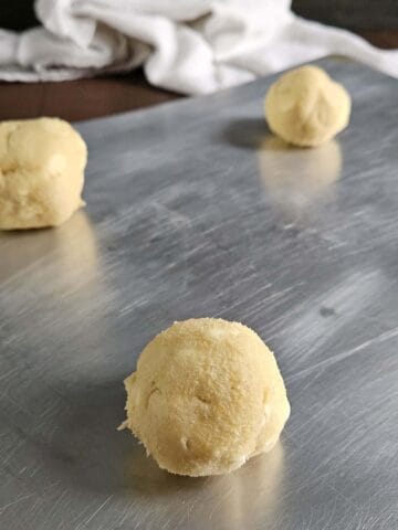 Three lemon cookie dough balls on a light-colored baking sheet.