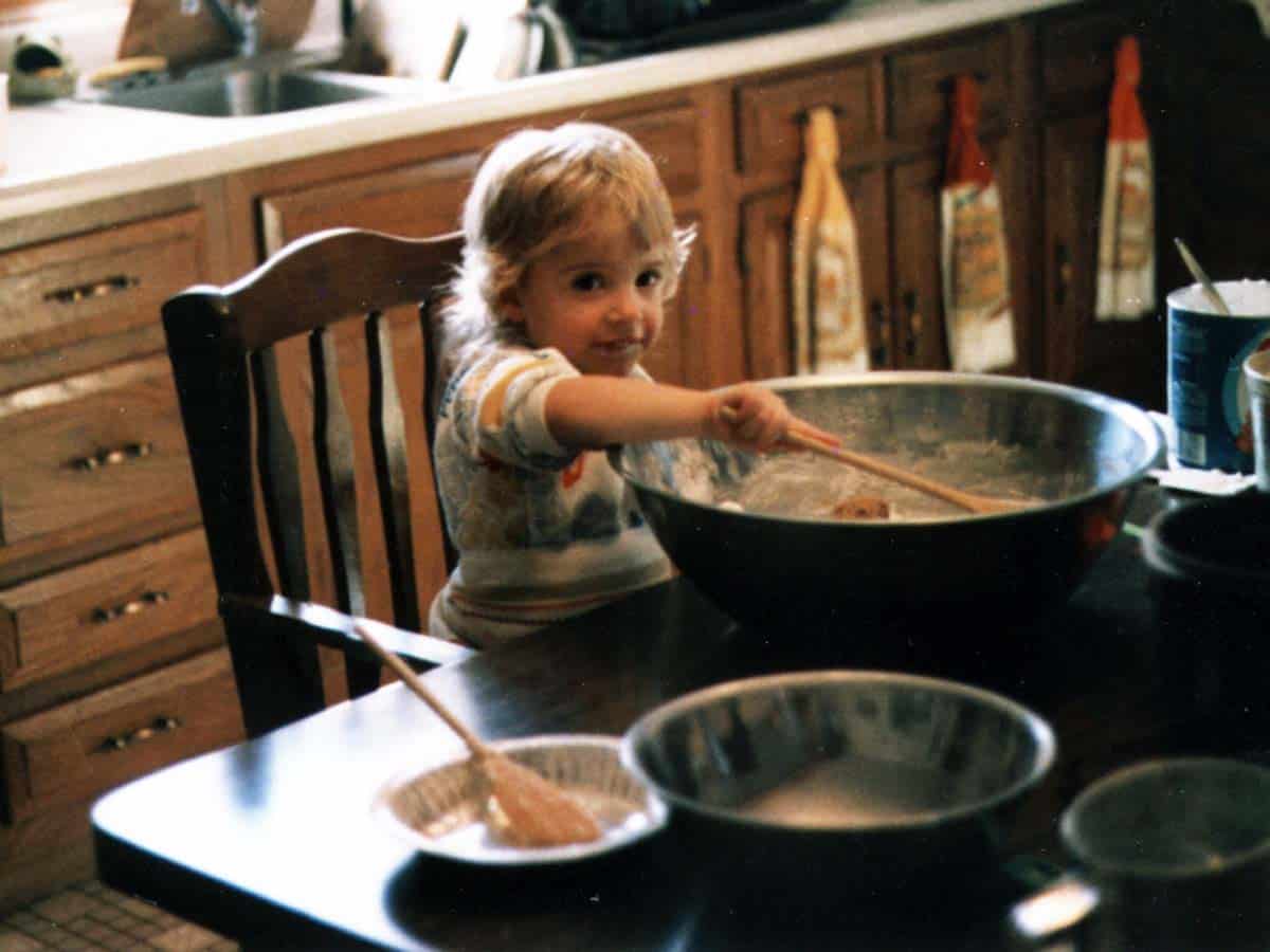 Young girl stirring cookie dough in a metal bowl.