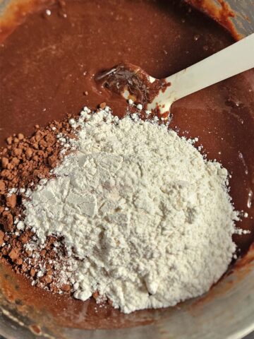 Brownie batter in a glass bowl topped with flour and cocoa powder.