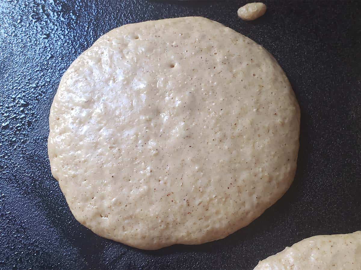 Oatmeal pancake cooking on an electric griddle.