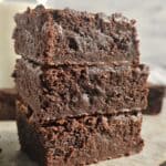 A stack of three brownies on parchment paper.