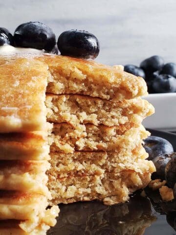Stack of oatmeal sourdough pancakes on a black plate topped with blueberries.