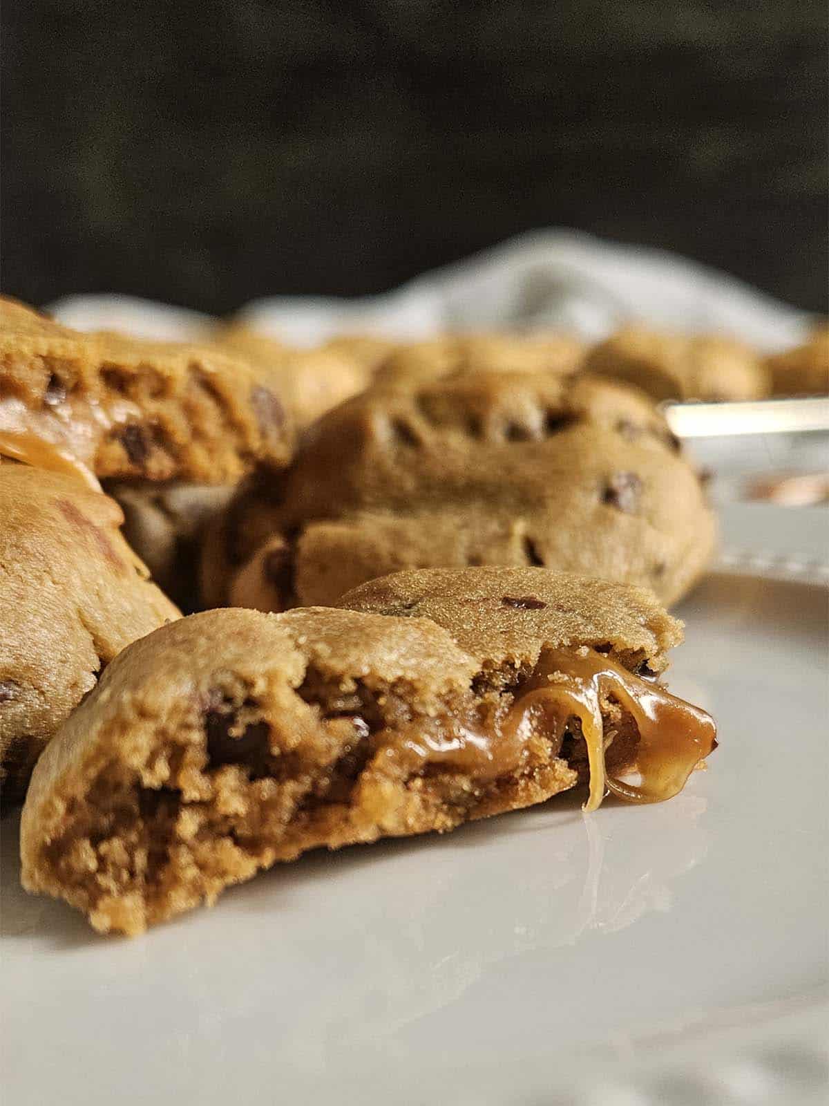 Half a peanut butter chocolate chip cookie with caramel oozing out on a white plate.