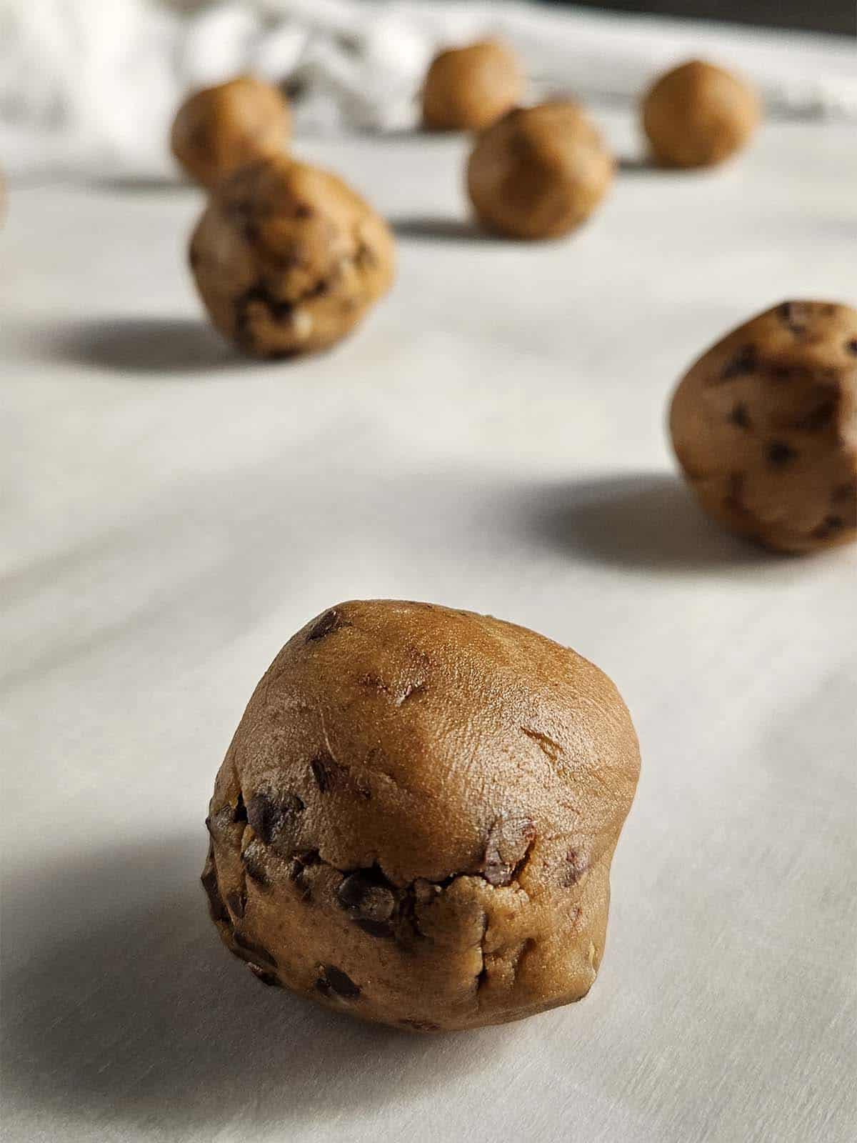 Seven cookie dough balls on parchment paper.