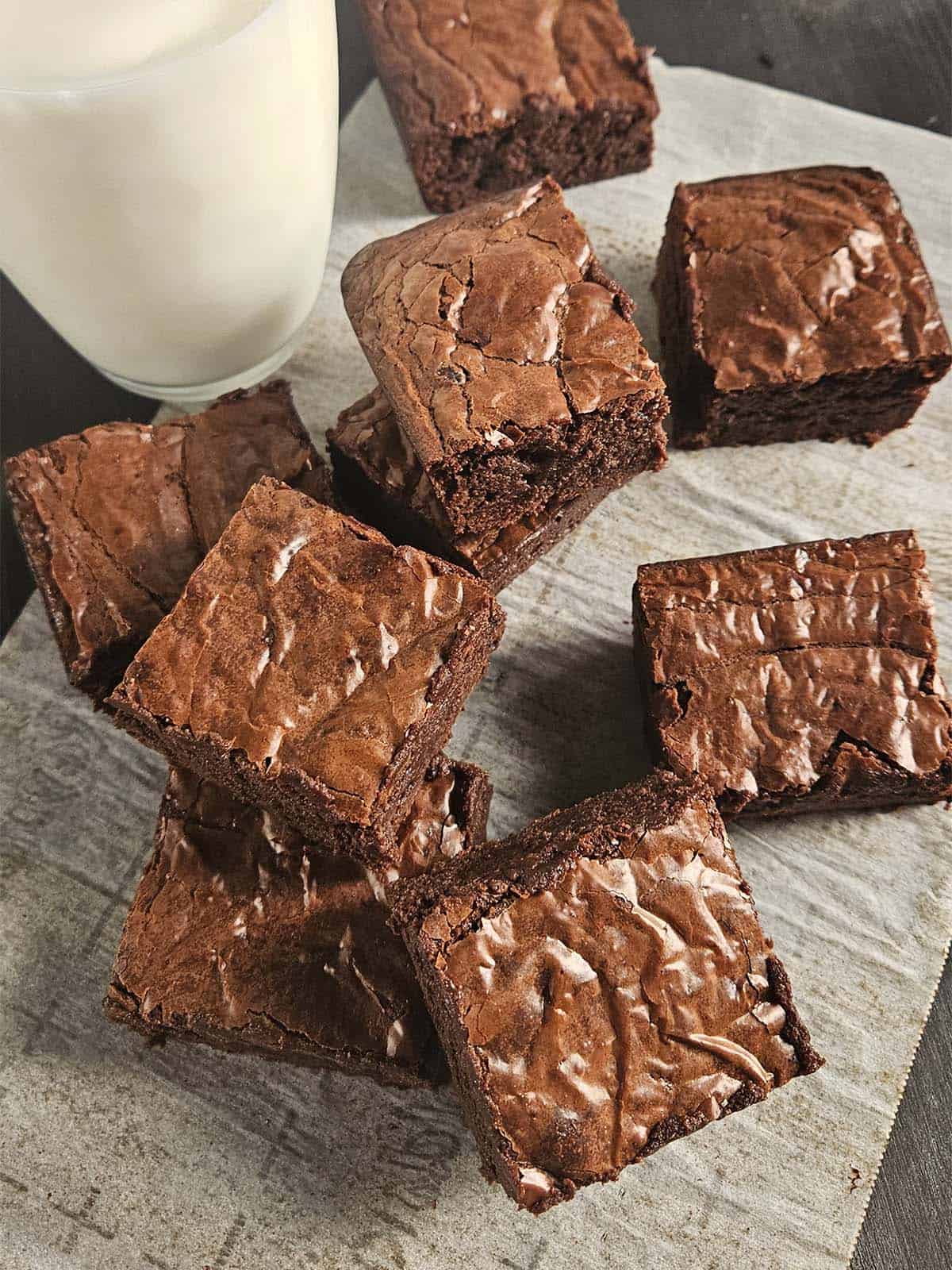 Brownies stacked on parchment paper next to a glass of milk.