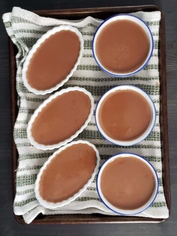 Six ramekins filled with Nutella custard in a towel-lined baking pan.