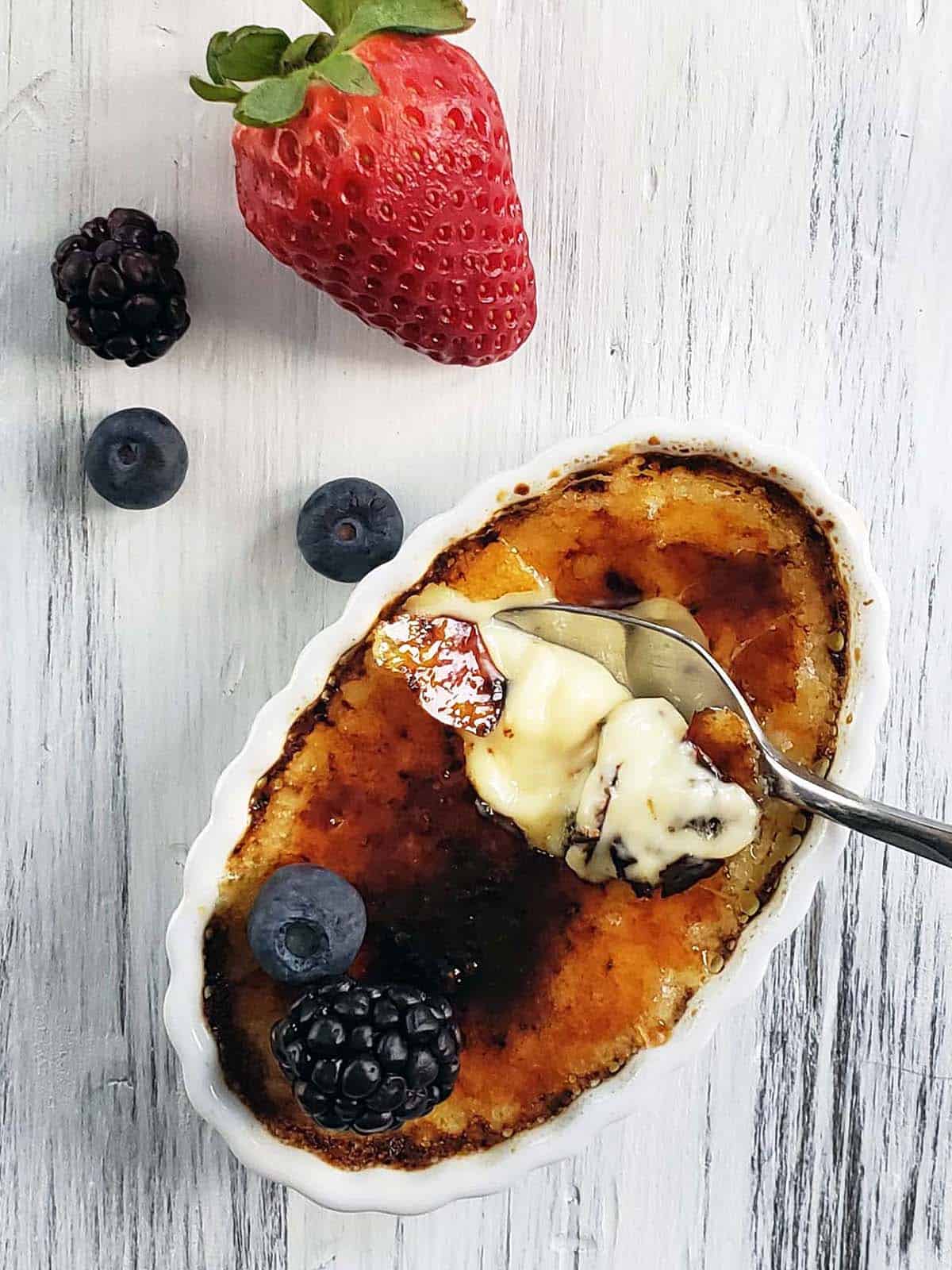 Vanilla creme brulee topped with berries with bite missing.