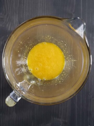Whisked egg yolks in a glass measuring cup.