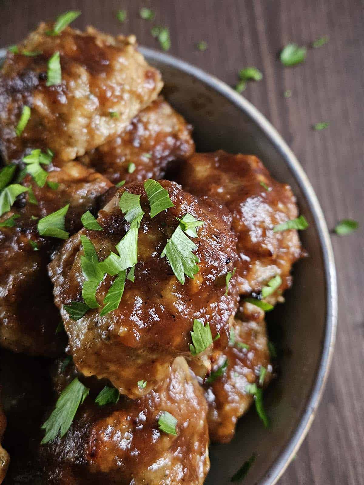 Meatballs covered in sauce and chopped parsley in a light-colored bowl.