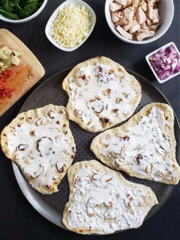 Four flatbreads on a pizza pan topped with cream cheese.