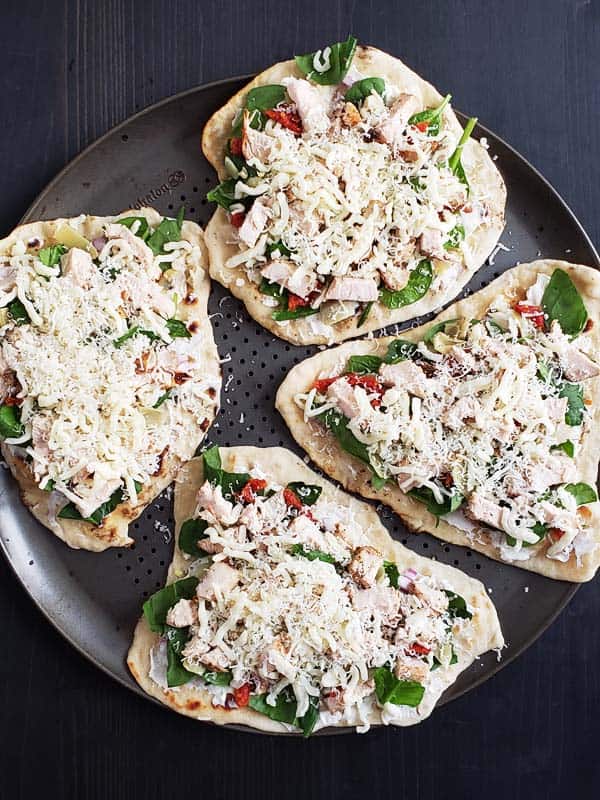 Four uncooked chicken artichoke flatbreads on a pizza pan.