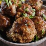 Meatballs covered in sauce and chopped parsley in a light-colored bowl.